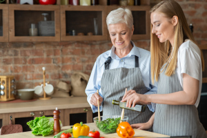 Eine jüngere und eine ältere Frau geben Öl zu einem Salat Eine jüngere und eine ältere Frau geben Öl zu einem Salat