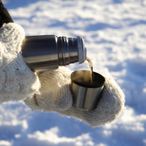 Hände in Handschuhen halten eine Thermoskanne Hände in Handschuhen halten eine Thermoskanne