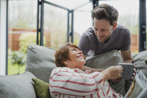Eine Seniorin auf dem Sofa bekommt von einem Mann eine Tasse Tee gereicht Eine Seniorin auf dem Sofa bekommt von einem Mann eine Tasse Tee gereicht
