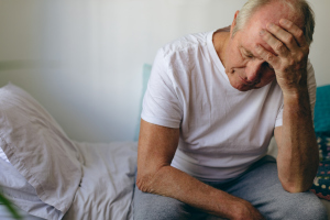 Gestresster älterer Mann auf dem Bett sitzend Gestresster älterer Mann auf dem Bett sitzend