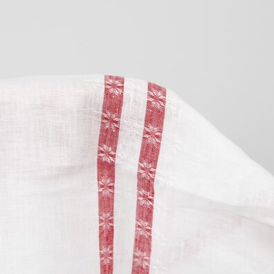 Baltas lininis audinys su raudonomis raštuotomis juostelėmis abiejuose kraštuose