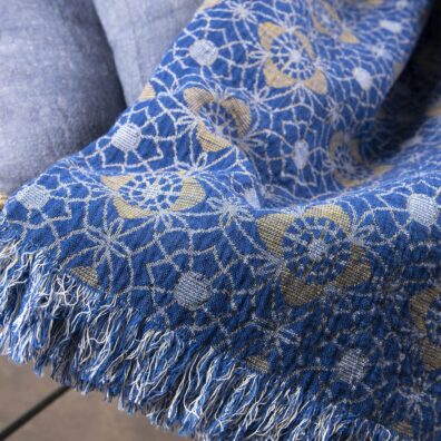 Mėlyno lininio pledo su gėlėtu raštu audinio vaizdas iš arti.