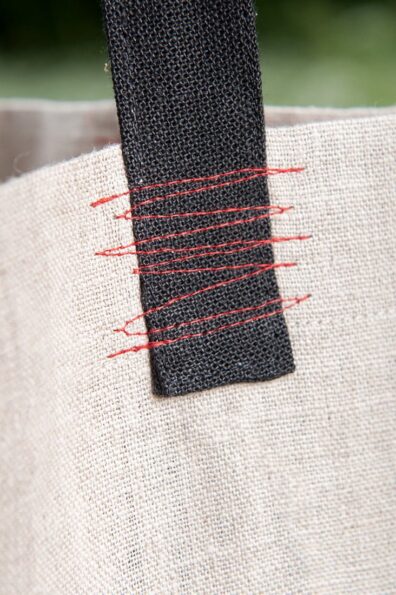 Pilkos lininės rankinės juodos rankenos sutvirtintos raudonų siūlių zigzagais