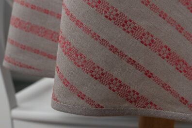 Pilka lino-medvilnės staltiesė raudonais raštuotais dryžiais, apvali, ovali.