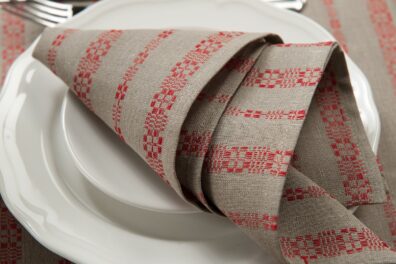 Pilka lino-medvilnės servetėlė raudonomis raštuotomis juostelėmis.