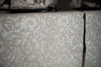 Puslininis raštuotas stalo takelis, kuriame suausti balti, pilki, sidabrinės spalvos verpalai