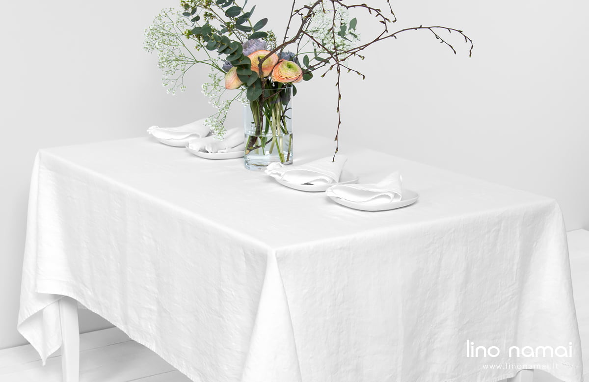 Balta lininė staltiesė su gėlėmis ant jos, pavyzdys vestuvių papuošimui.