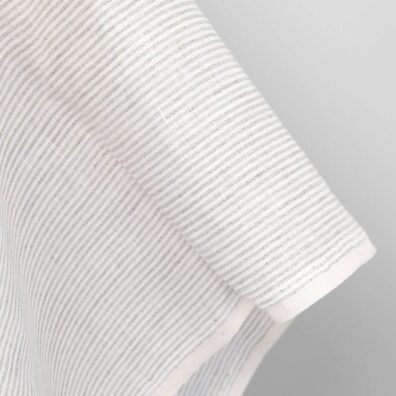 Mlecznobiałe tło tkaniny lnianej zostało wytkane w pionowe paski z przędzy o barwie szarego, niebarwionego lnu