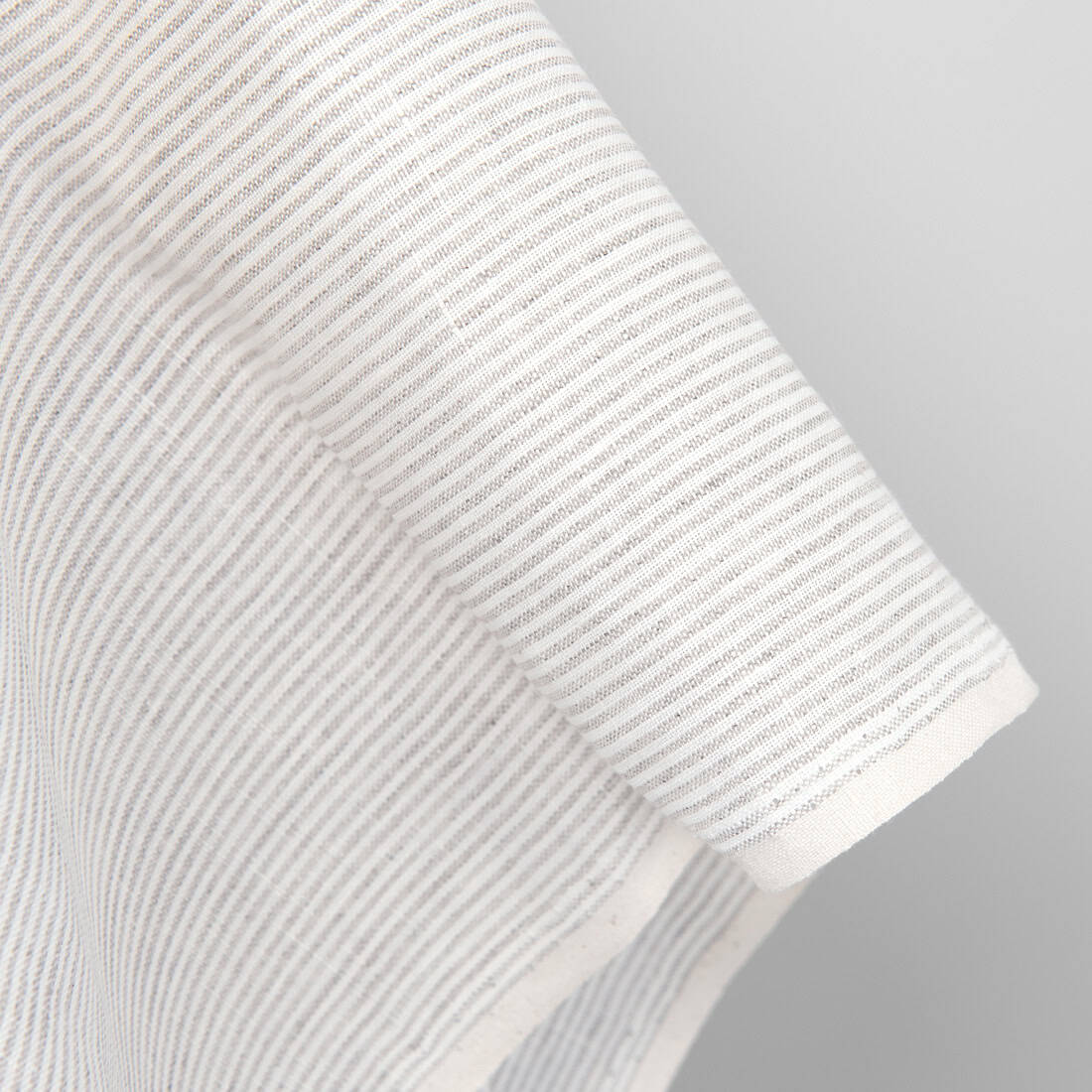 Mlecznobiałe tło tkaniny lnianej zostało wytkane w pionowe paski z przędzy o barwie szarego, niebarwionego lnu