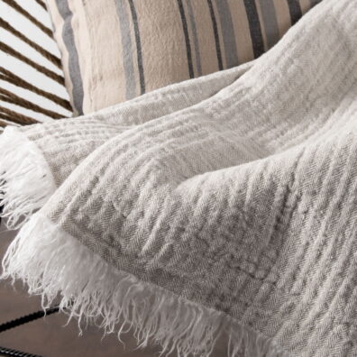 Jasny szary pled ozdobiony na krótszych brzegach frędzelkami 5 cm.