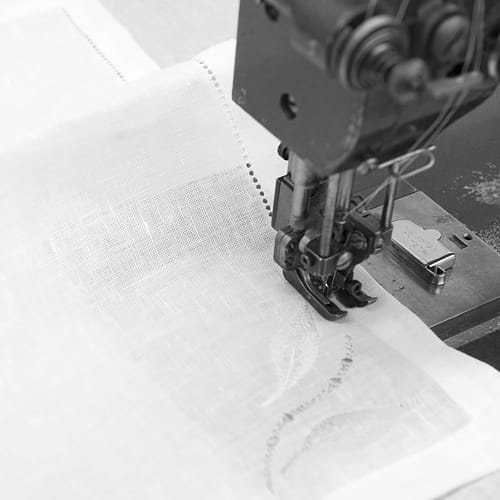 Szycie białych lnianych serwetek.