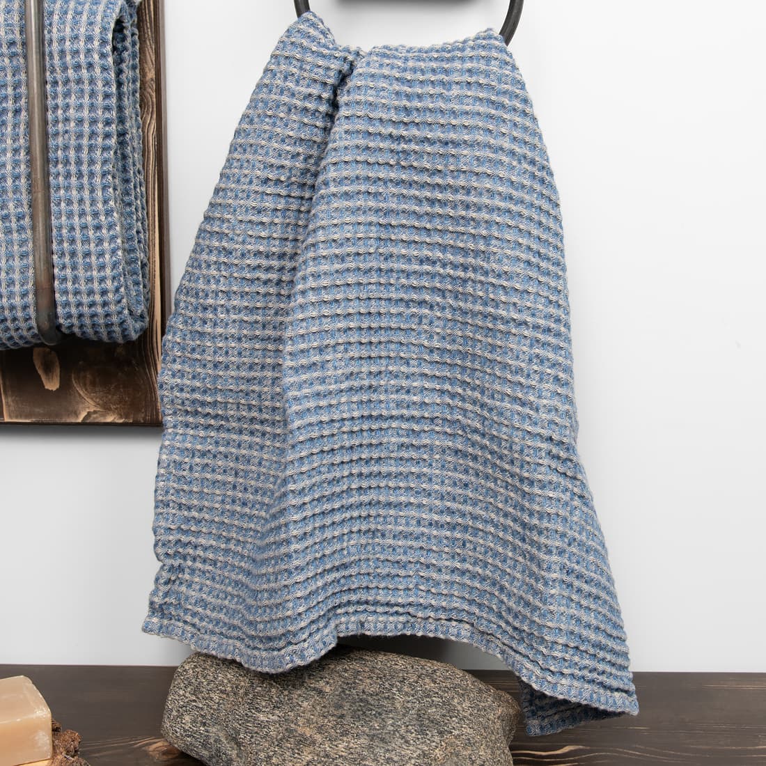 Ręcznik wytkany w melanżu z szarej w piasek i dżinsowo niebieskiej przędzy.