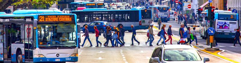 Via Carducci a Trieste, con numerosi autobus e molte persone che attraversano la strada.