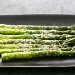 Bord met een portie in de oven gebakken asperges met gesmolten Parmezaanse kaas.