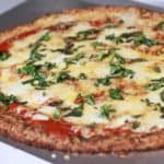 Een heerlijke koolhydraatarme bloemkoolpizza belegd met tomatensaus en mozzarella.