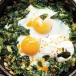 Een pan vol met gebakken eieren met spinazie, prei, lente-ui en een saus van yoghurt en knoflook.