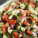 Schaal met Israëlische salade bestaande uit komkommers, tomaat, rode ui en kruiden.