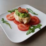 Portie kipfilet met plakjes tomaat en courgettesaus gegarneerd met zongedroogde tomaat en rucola.