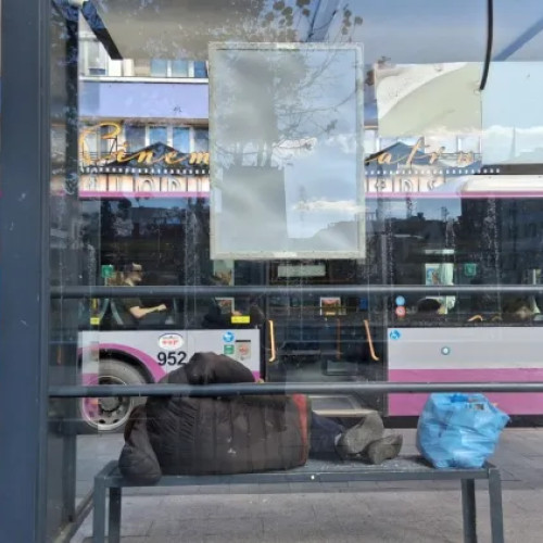 Un om al străzii îngheață pe o bancă în stația de autobuz din Piața Mihai Viteazu