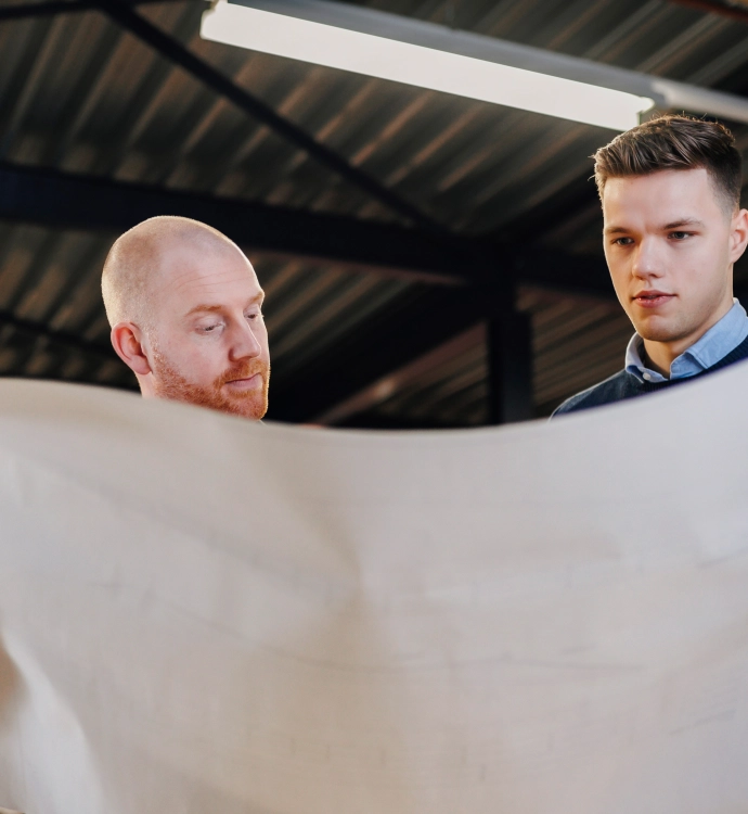 Twee mannen die gefocust en geïnteresseerd naar plotterpapier kijken in een magazijn.