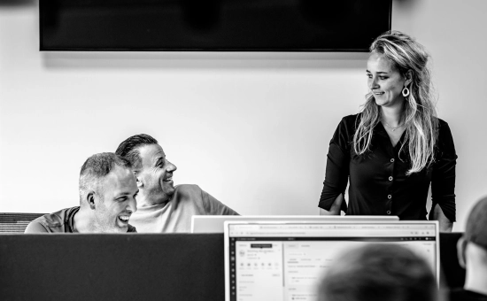 Drie medewerkers op enthousiaste wijze in gesprek met elkaar in een werkruimte.