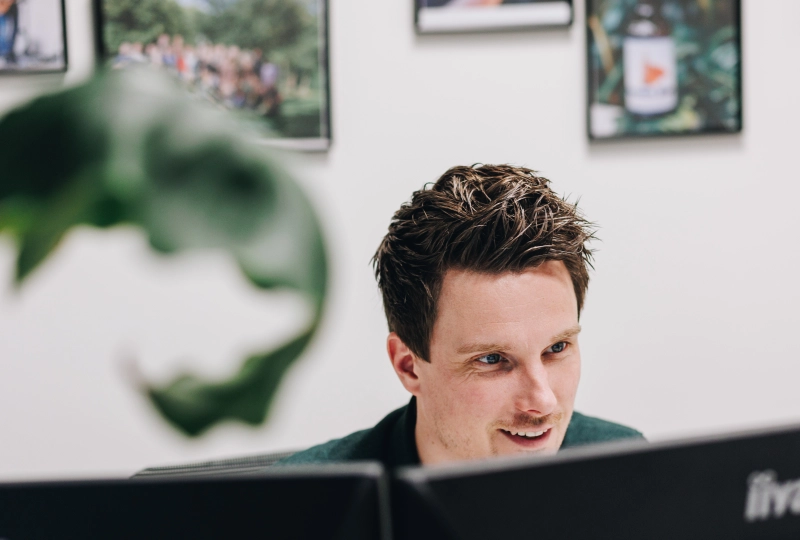 Een man die lachend en geïnteresseerd naar zijn computer scherm kijkt, tijdens zijn werkzaamheden.