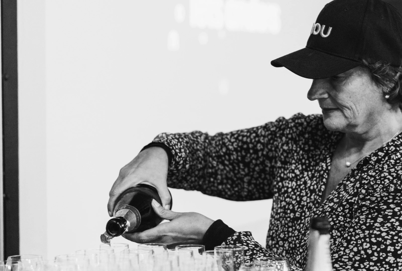 Een mevrouw met een zwarte pet op die meerdere glazen met champagne vult.