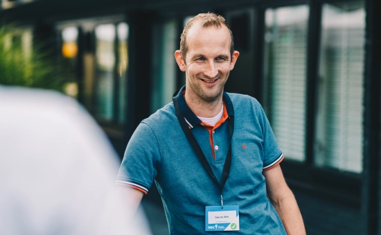 Een lachende man die onwetend op de foto is gezet in een buitenomgeving.