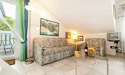 Blick in den Wohnbereich und zum Austritt zum Balkon. Couch und Sessel können für die Aufbettung ausgezogen werden.