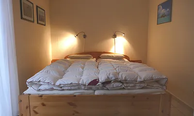 Schlafzimmer mit Doppelbett, Schrank, Korbstuhl, Spiegel