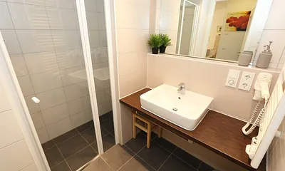 Badezimmer mit ebenerdiger Dusche, Waschbecken, WC, Kosmetikspiegel, festinstallierter Haarfön und Handtuchheizkörper