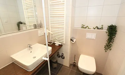 Badezimmer mit ebenerdiger Dusche, Waschbecken, WC, Kosmetikspiegel, festinstallierter Haarfön und Handtuchheizkörper