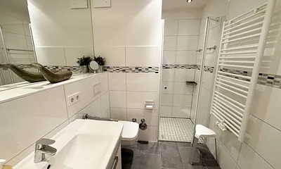 Badezimmer mit ebenerdiger Dusche, Waschbecken, Kosmetikspiegel, Fön, WC und Handtuchheizkörper