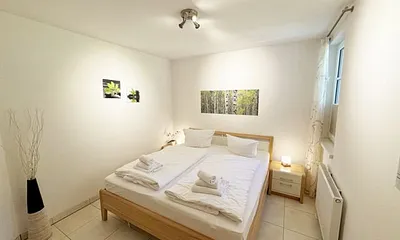 Schlafzimmer mit komfortablem Doppelbett (1,80 m x 2,00 m), hochwertigen Matratzen, Nachttischkonsolen, 4-trg. Drehtürenkleiderschrank (Kernbuche mit Lack creme Fronten), Verdunklungsplissees & TV