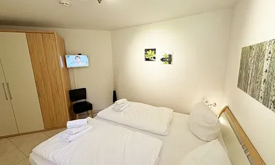 Schlafzimmer mit komfortablem Doppelbett (1,80 m x 2,00 m), hochwertigen Matratzen, Nachttischkonsolen, 4-trg. Drehtürenkleiderschrank (Kernbuche mit Lack creme Fronten), Verdunklungsplissees & TV