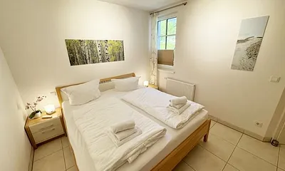 Schlafzimmer mit komfortablem Doppelbett (1,80 m x 2,00 m), hochwertigen Matratzen, Nachttischkonsolen, 4-trg. Drehtürenkleiderschrank (Kernbuche mit Lack creme Fronten), Verdunklungsplissees & TV