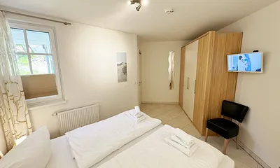 Schlafzimmer mit komfortablem Doppelbett (1,80 m x 2,00 m), hochwertigen Matratzen, Nachttischkonsolen, 4-trg. Drehtürenkleiderschrank (Kernbuche mit Lack creme Fronten), Verdunklungsplissees & TV
