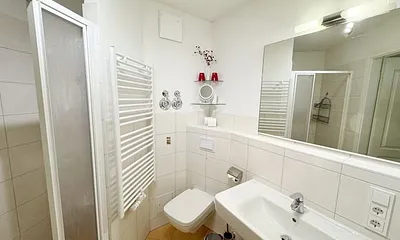 Badezimmer mit ebenerdiger Dusche, Waschbecken, WC und Handtuchtrockner