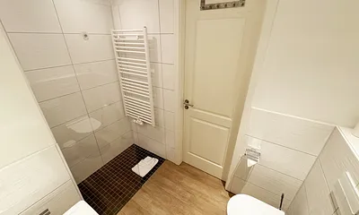 Badezimmer mit ebenerdiger Dusche, Waschbecken, WC und Handtuchheizkörper