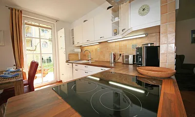 angrenzender Küchenbereich mit Kühlschrank, Induktionsstromherd, Dunstabzugshaube, Spülmaschine, Toaster, Wasserkocher, Espressomaschine, Rührgerät sowie weitere Helfer