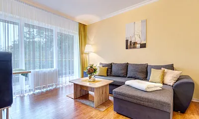 Wohnzimmer mit Schlafcouch, Essplatz und Flat-TV sowie Balkon
