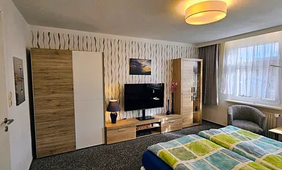1. Schlafzimmer mit kleiner Anbauwand, Kleiderschrank, Sat-TV,  2 Clubsessel und Tisch, Verducklungsvorhang 