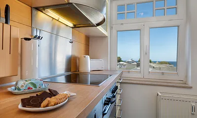 Geschirr, Besteck und Küchengeräte sind überwiegend von namhaften Marken. Auch im Küchenfenster sehen Sie das Meer.