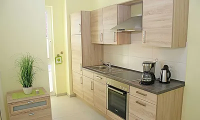 angrenzende Küchenzeile mit Ceranfeld, Geschirrspüler, Kühlschrank mit Gefrierfach, Backofen, Wasserkocher, Kaffeemaschine, Toaster und diverse Küchenutensilien