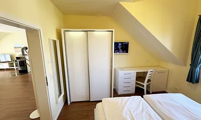 Schlafzimmer mit Doppelbett (1,80 m x 2,00 m mit Komforthöhe), Nachttischablagen, Kleiderschrank, Schreibtisch und Flachbild-TV