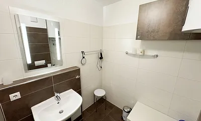 Badezimmer mit Dusche, WC, Kosmetikspiegel, Fön, Waschbecken und Handtuchwärmeheizkörper