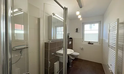 komfortables Badezimmer mit WC, Waschbecken, Fön, Dusche und Handtuchwärmeheizkörper