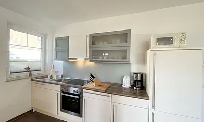 Küchenzeile mit Cerankochfeld, Backofen, Dunstabzugshaube, Kühlschrank mit Gefrierfach, Spülmaschine, Kaffeemaschine, Mikrowelle, Wasserkocher, Toaster und diverse Küchenutensilien