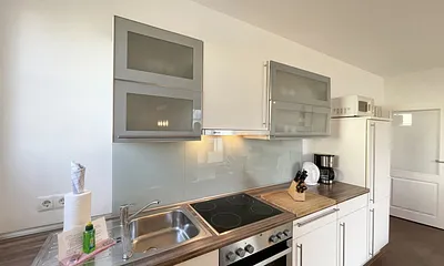 Küchenzeile mit Cerankochfeld, Backofen, Dunstabzugshaube, Kühlschrank mit Gefrierfach, Spülmaschine, Kaffeemaschine, Mikrowelle, Wasserkocher, Toaster und diverse Küchenutensilien