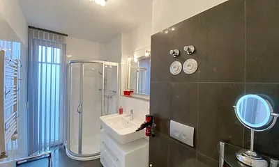 Badezimmer mit ebenerdiger Glasdusche, WC, beheizbaren Handtuchhalter, Fön, Kosmetikspiegel und modernen Waschplatz mit Beleuchtung